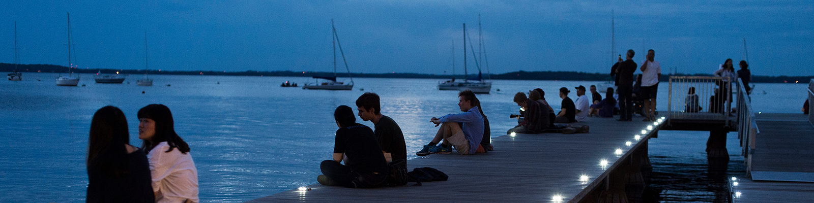 As dusk falls to nighttime, people relax on the Goodspeed Family Pier and take in a post-sunset view of the Memorial Union Terrace and Lake Mendota shoreline at the University of Wisconsin-Madison during a summer evening on June 14, 2014. (Photo by Jeff Miller/UW-Madison)
